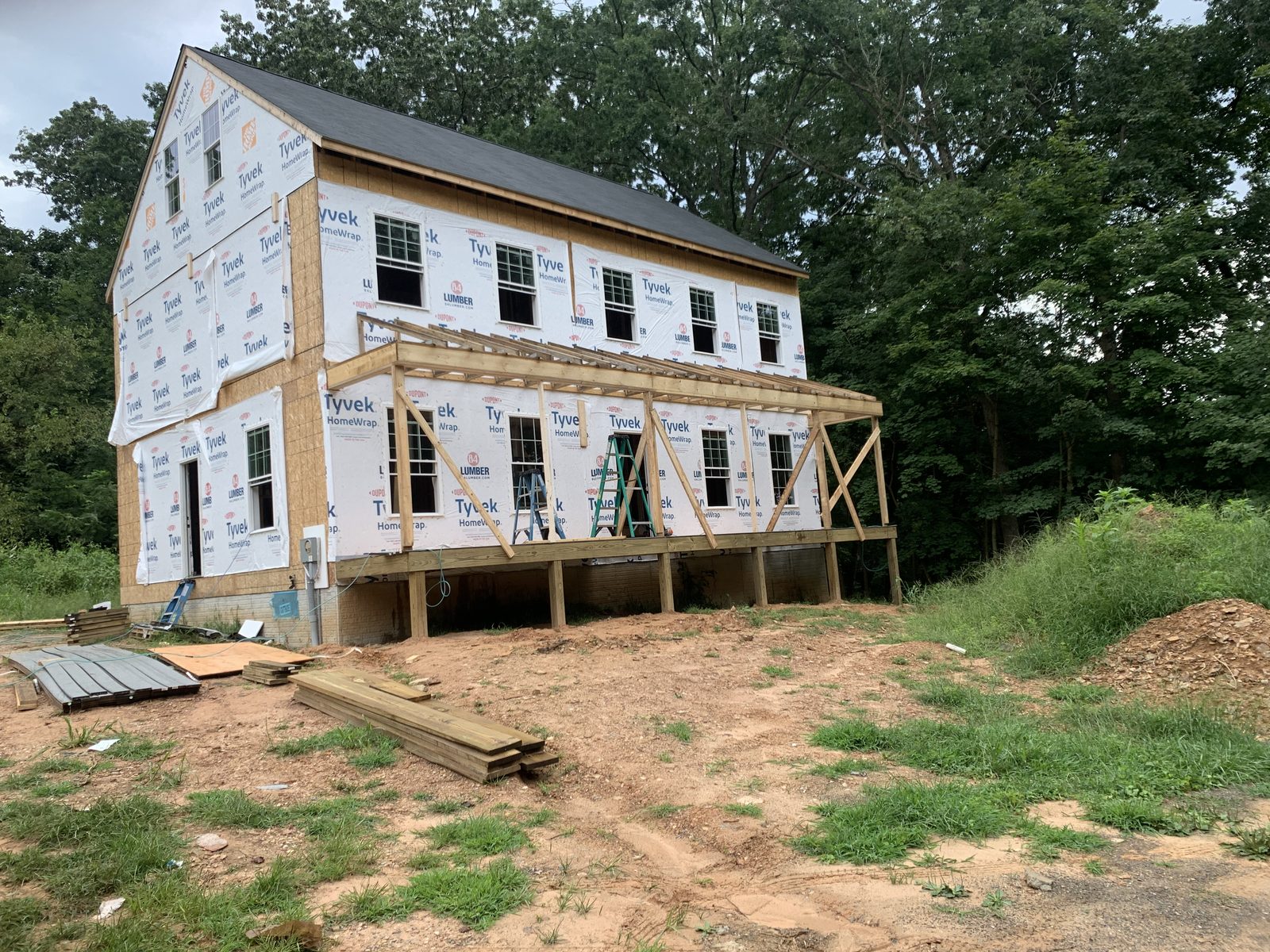 Barn-style house in wrap with a new porch roof being framed