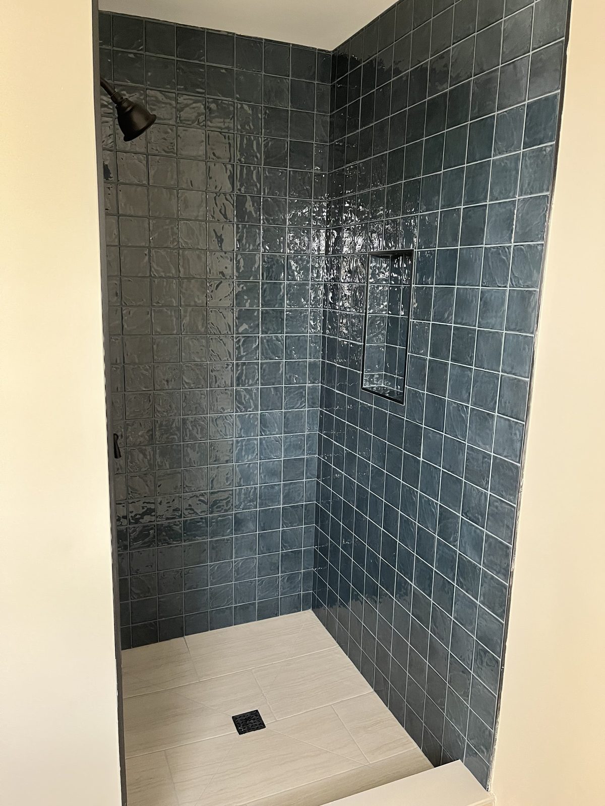 Walk-in shower in glossy blue-green tile with a recessed niche