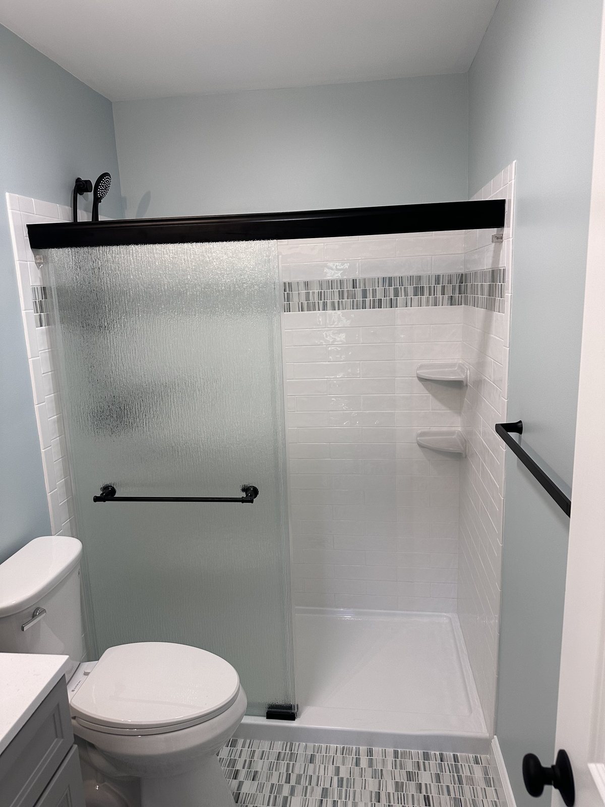 White subway shower with a mosaic band, corner shelves, and frosted glass