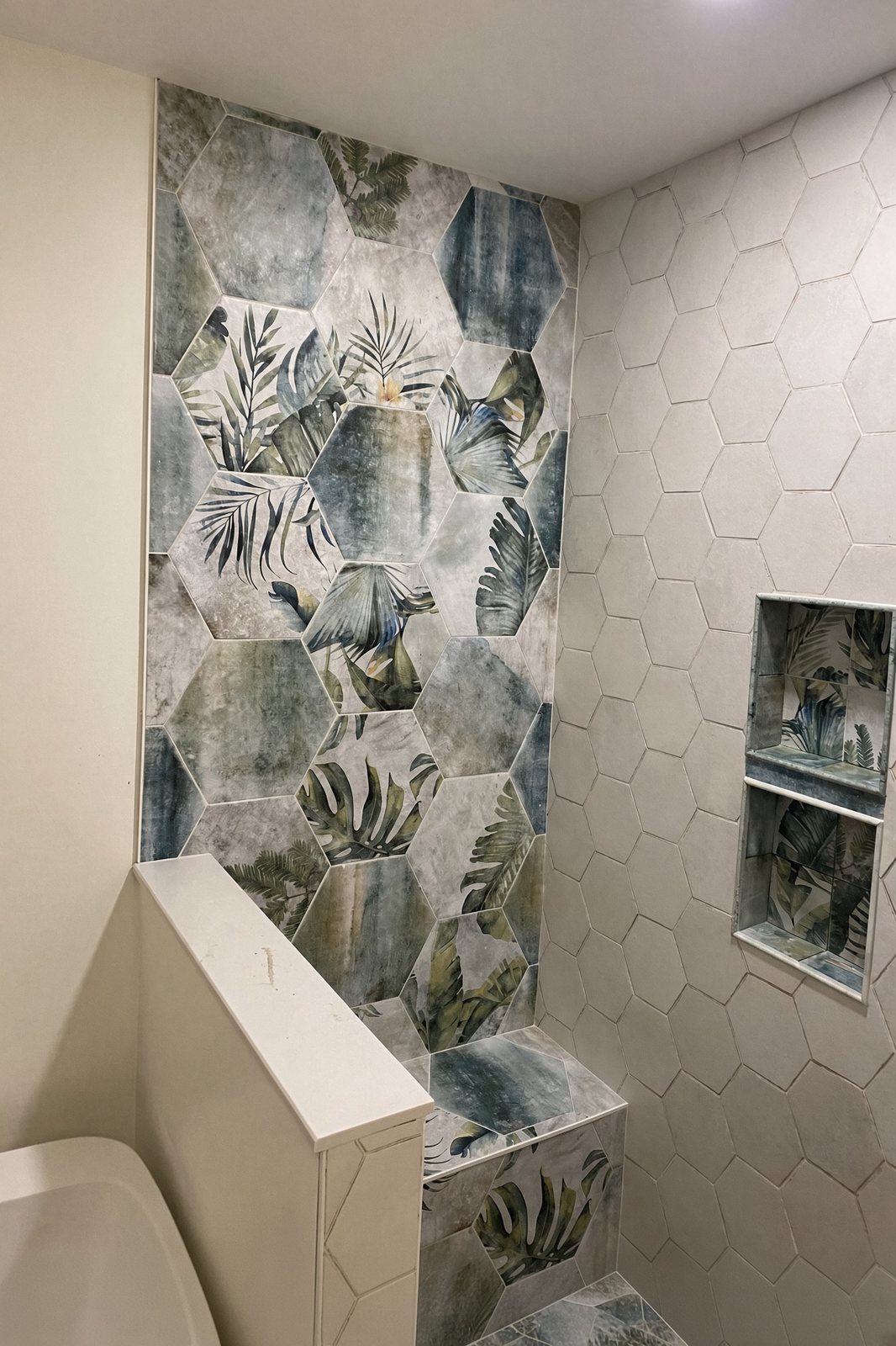 Shower in white hexagon tile with a tropical leaf feature wall, bench, and niche