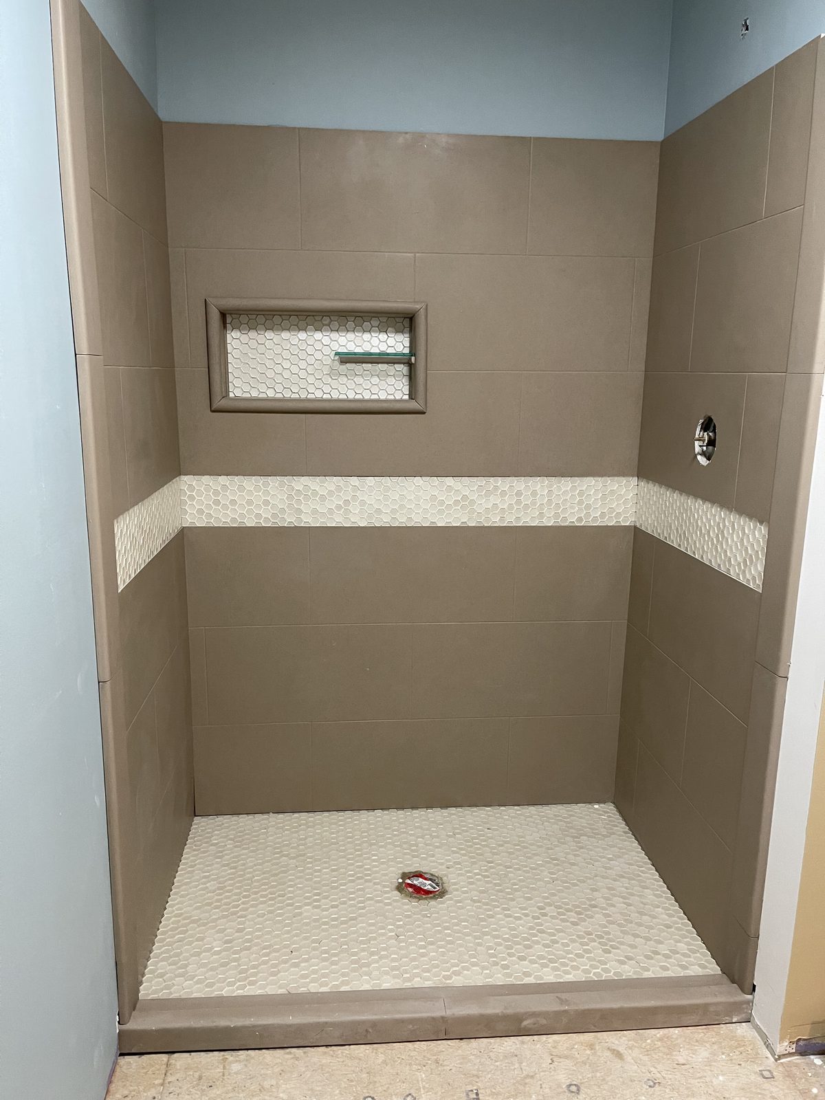 Shower with large tan tile, a hex-mosaic band, and hex floor