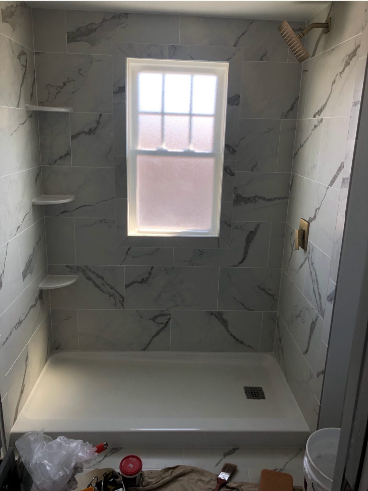 Marble-look tiled shower with a frosted window and brass fixtures
