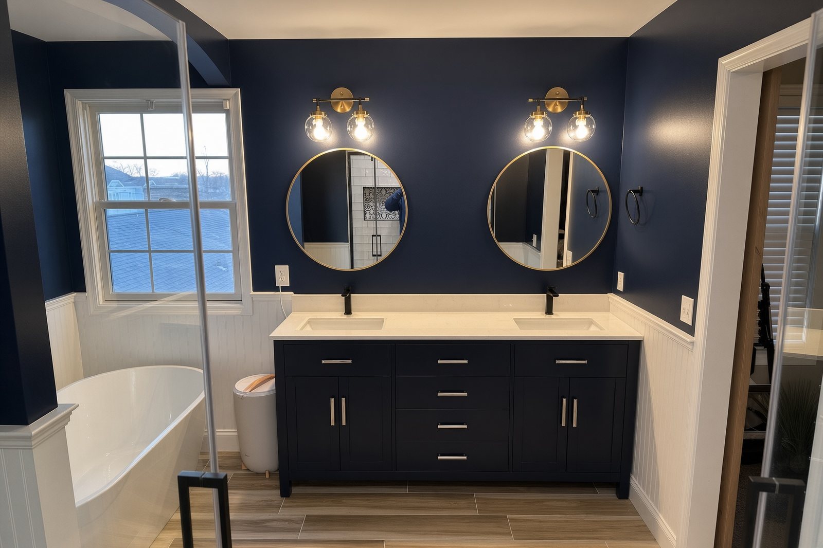 Navy double vanity with round gold mirrors and globe sconces