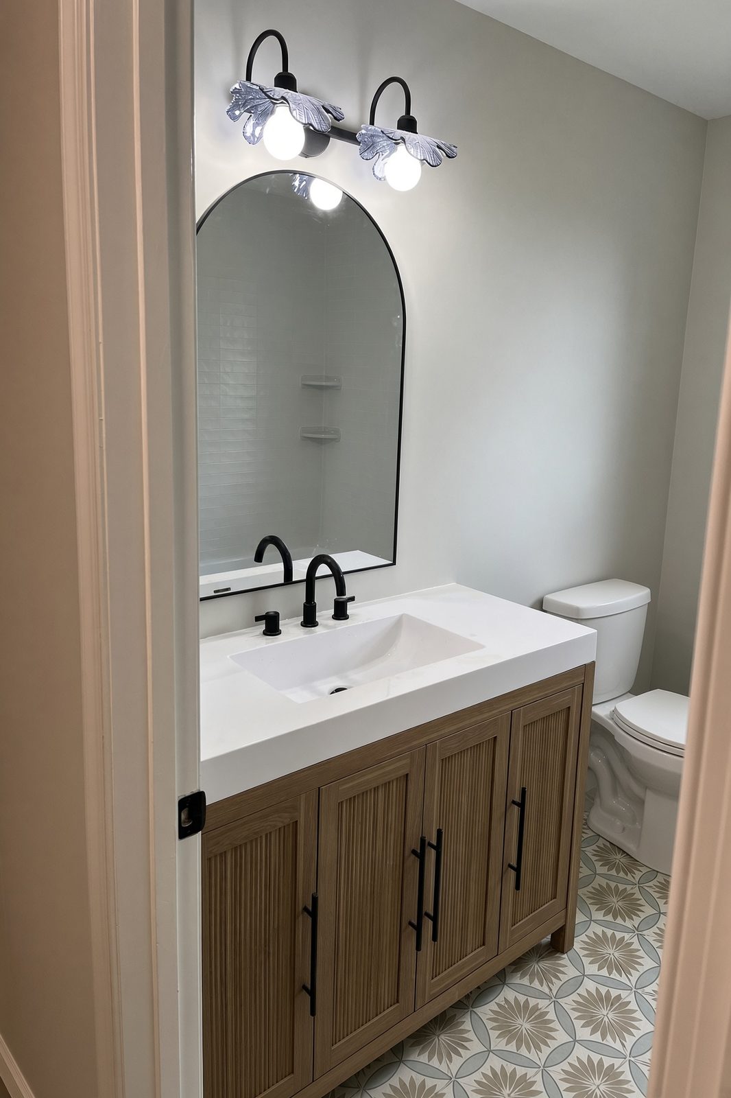 Hall bath with a light oak reeded vanity, black fixtures, and an arched mirror