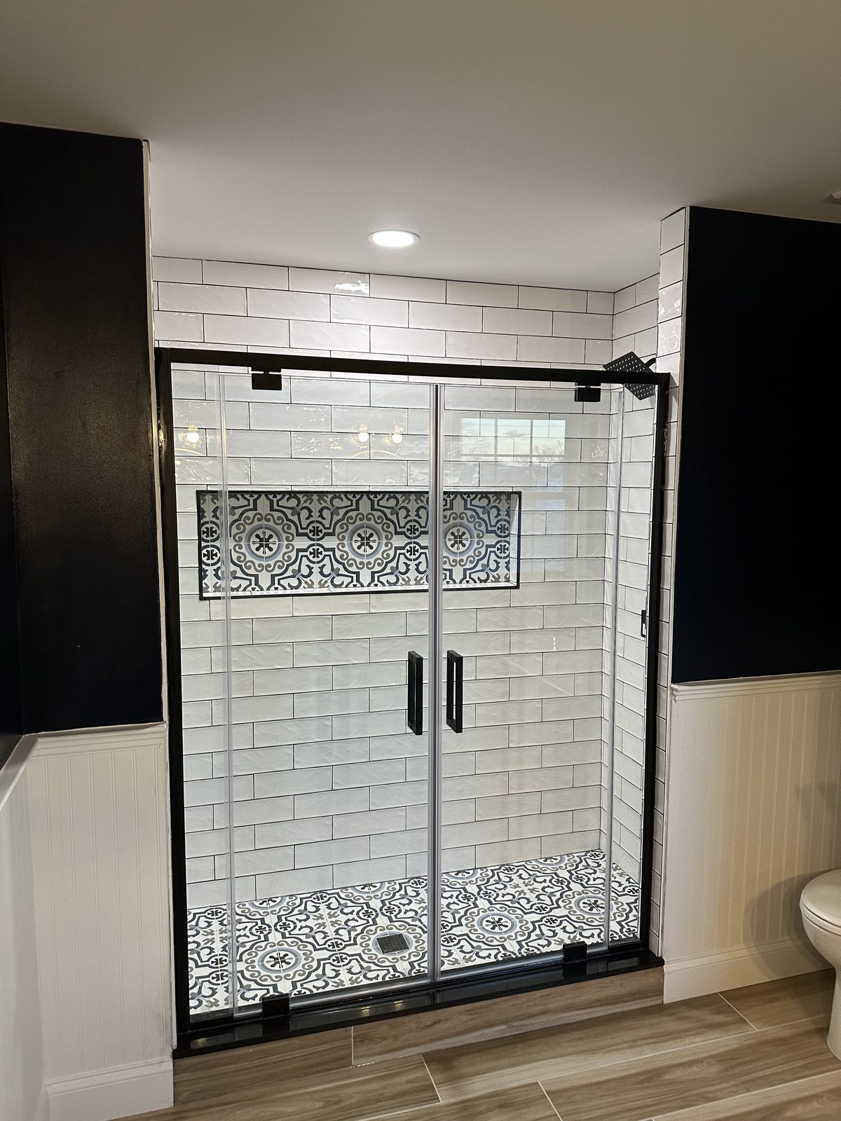 Finished glass shower with white subway tile and a patterned niche and floor