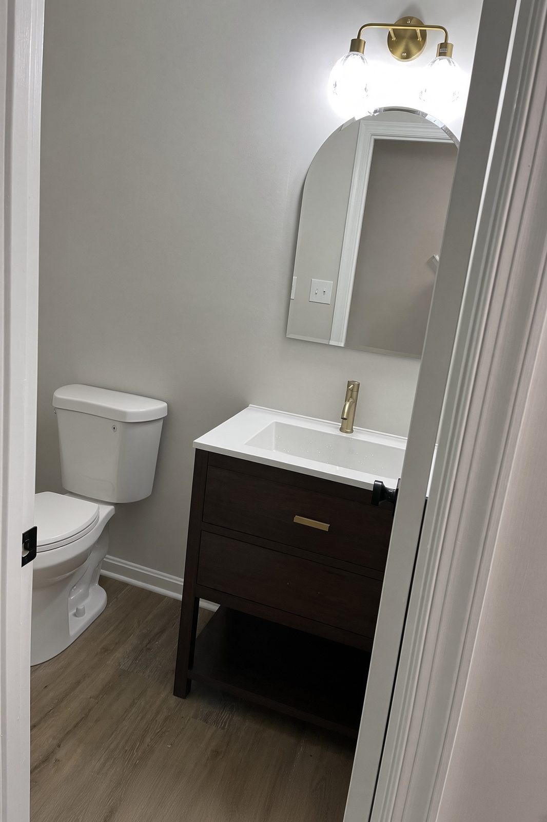 Powder room with a dark wood vanity, gold faucet, and arched mirror