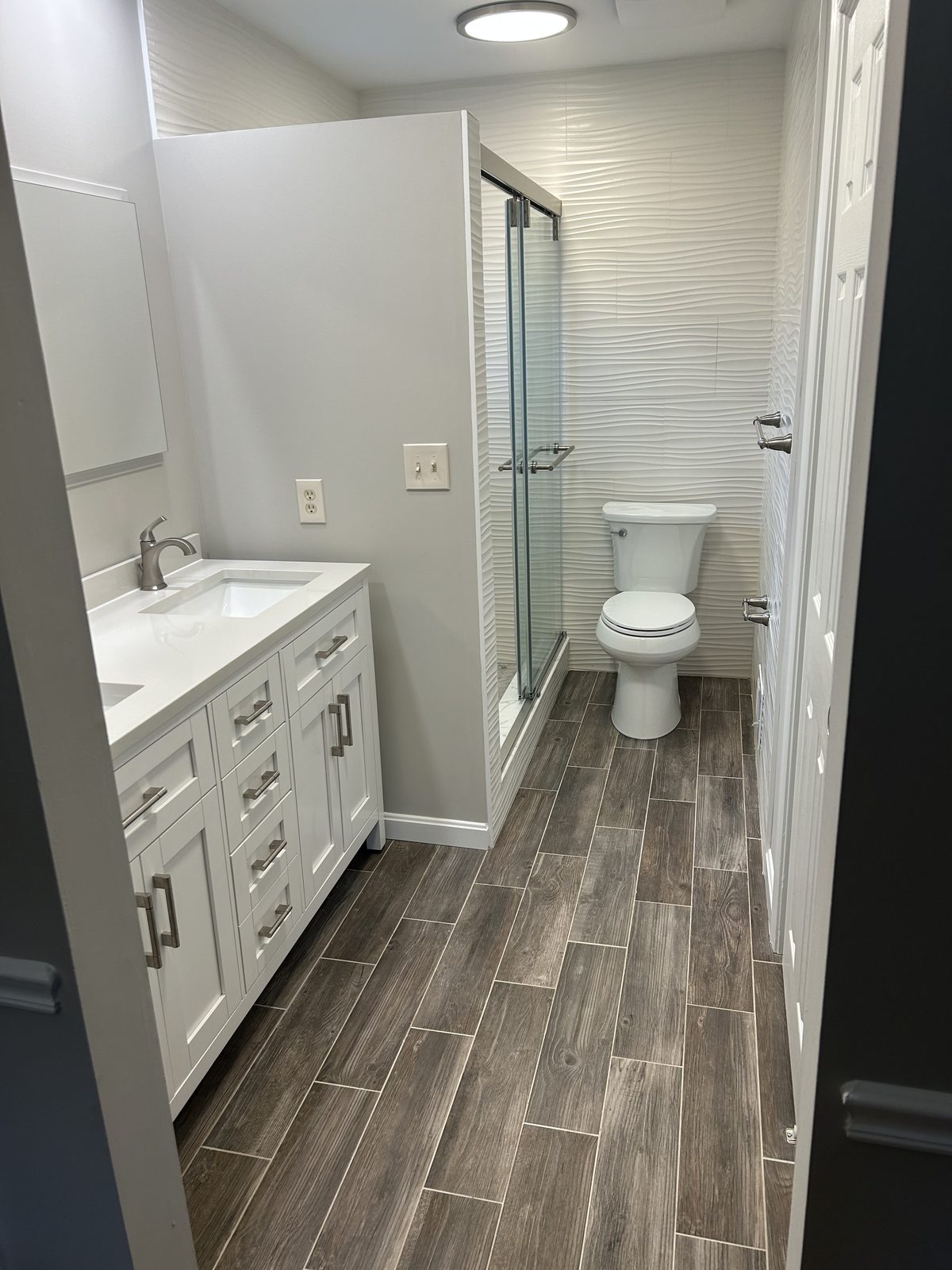 Finished hall bath with wavy wall tile, glass shower, and white vanity