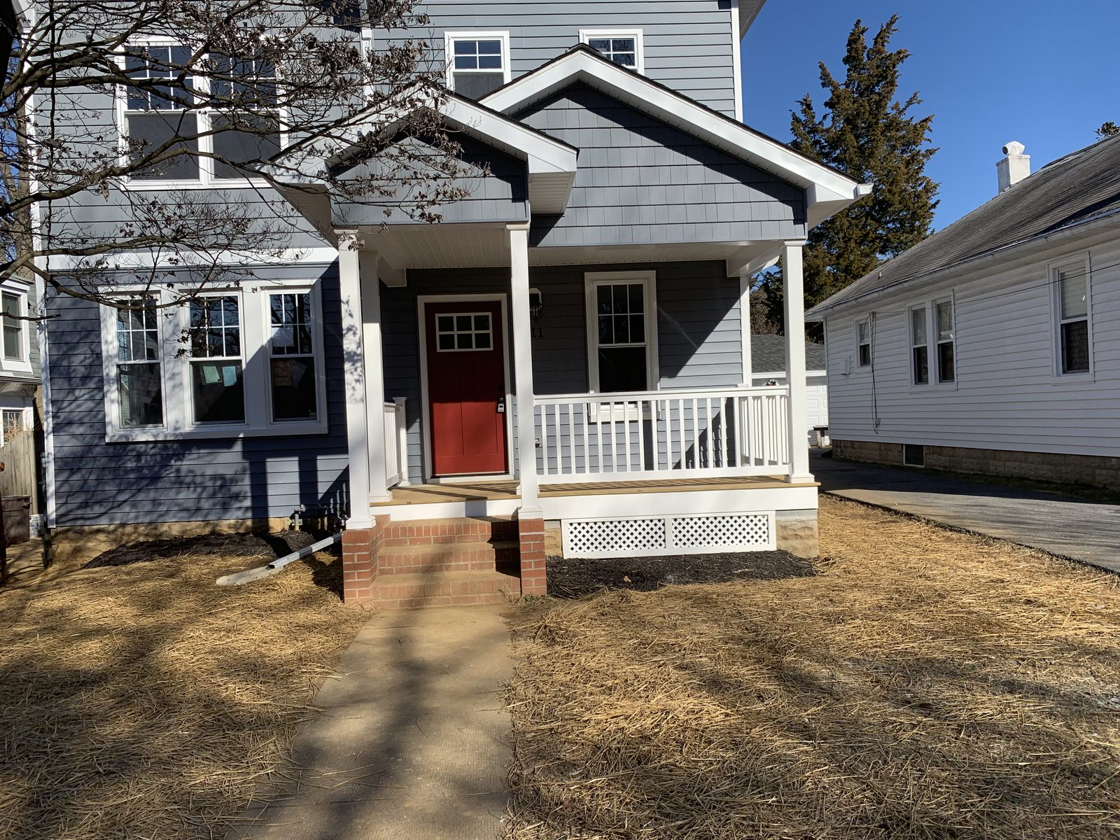 Finished gray house with a white porch and red front door