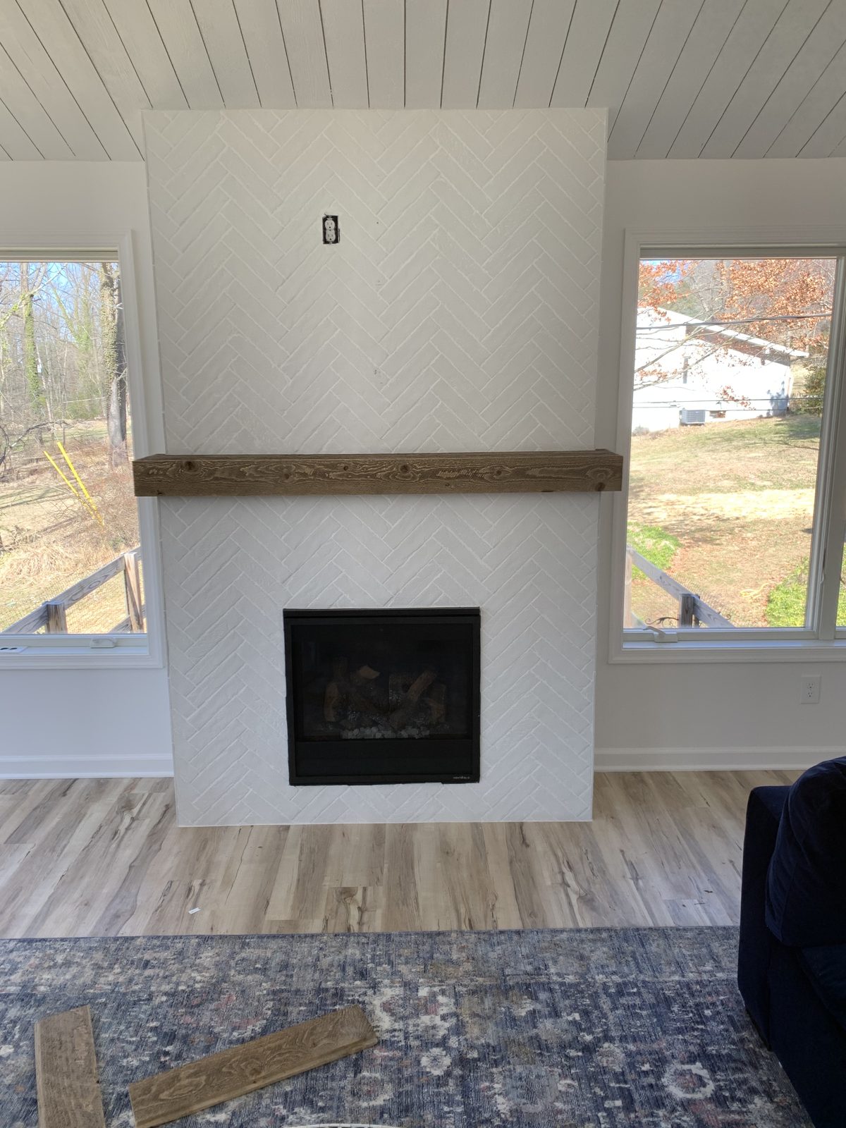 White herringbone fireplace with a thick wood mantel between two windows
