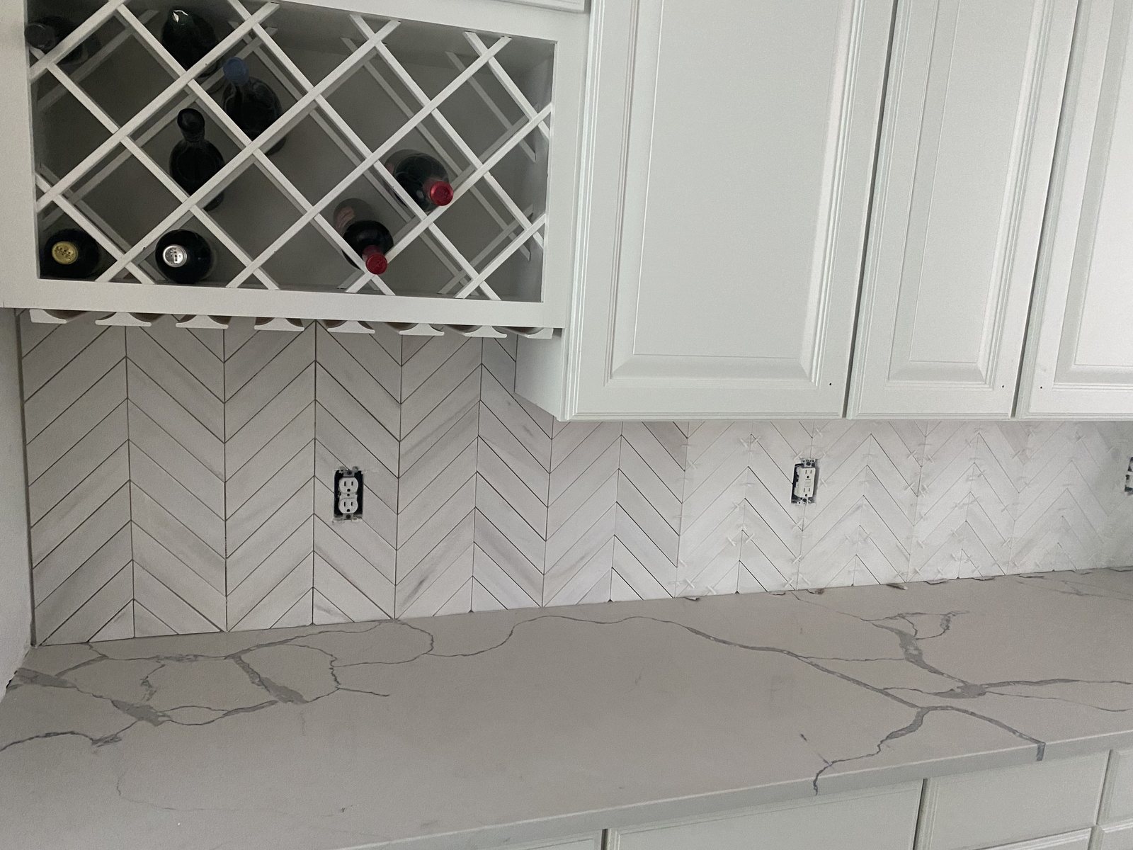 Built-in wine rack over a white herringbone tile backsplash and quartz counter