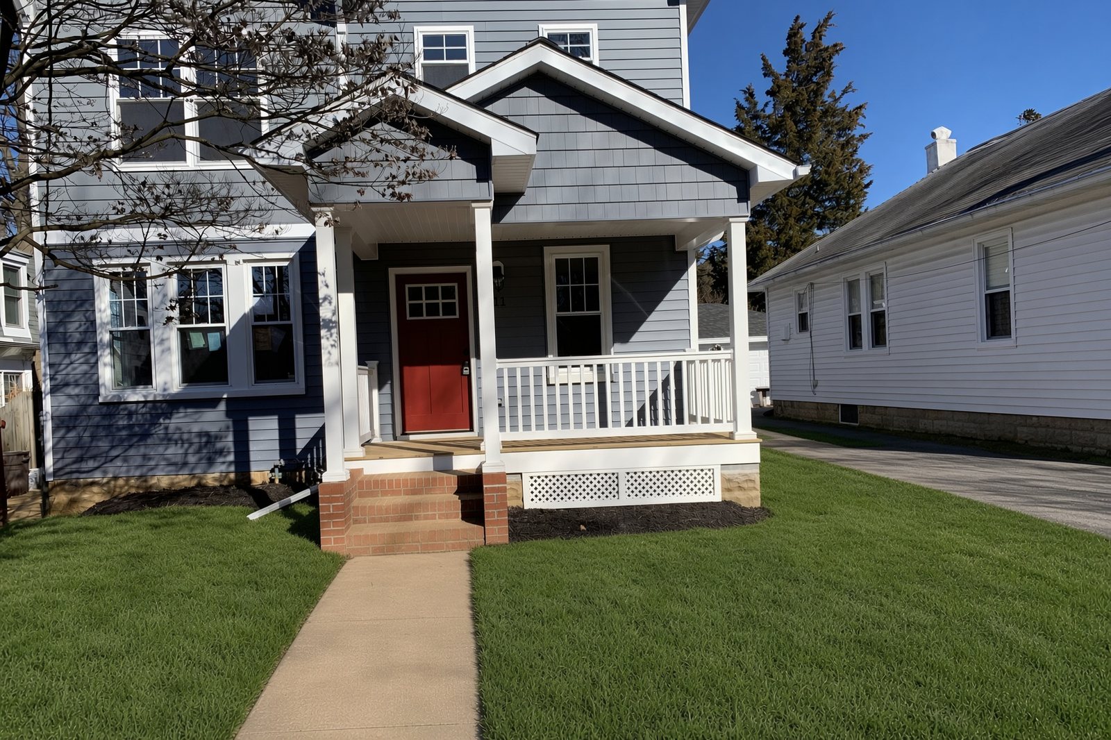 Gray two-story house with a white porch, brick steps, and a red front door
