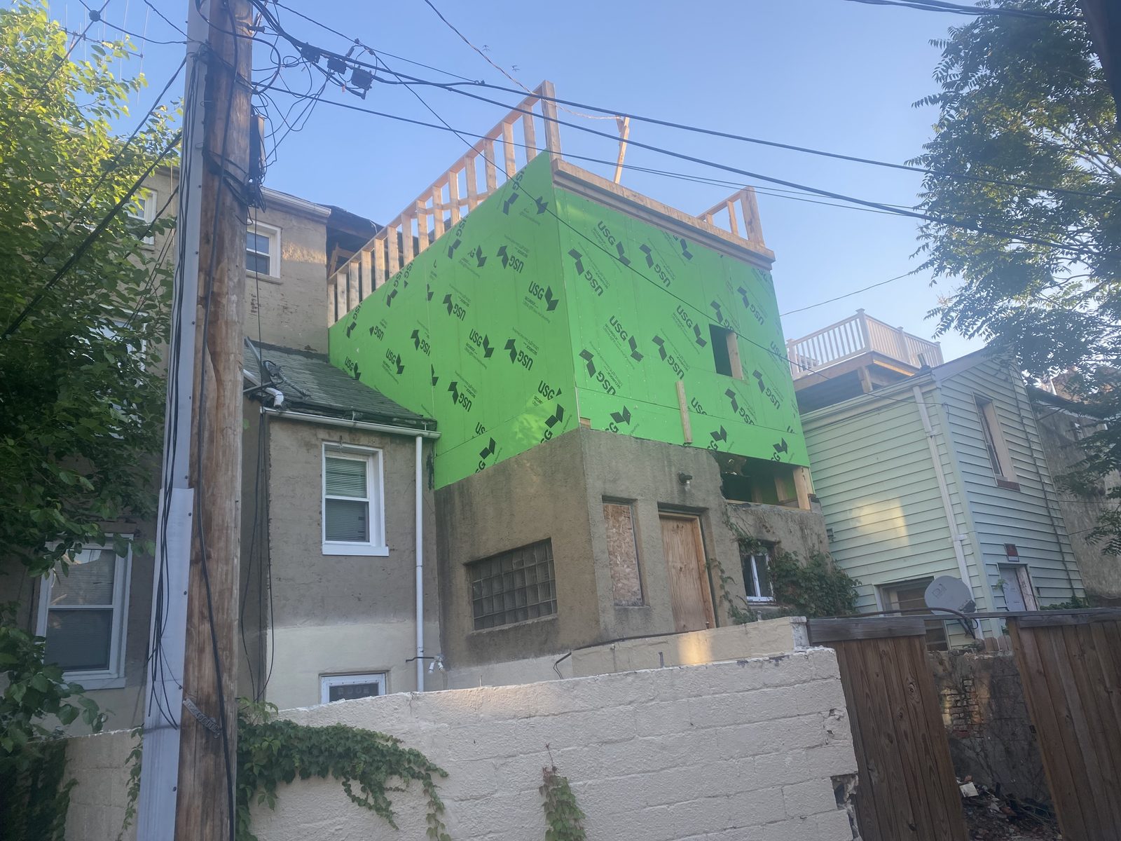 Urban row addition wrapped in green sheathing over an existing masonry house