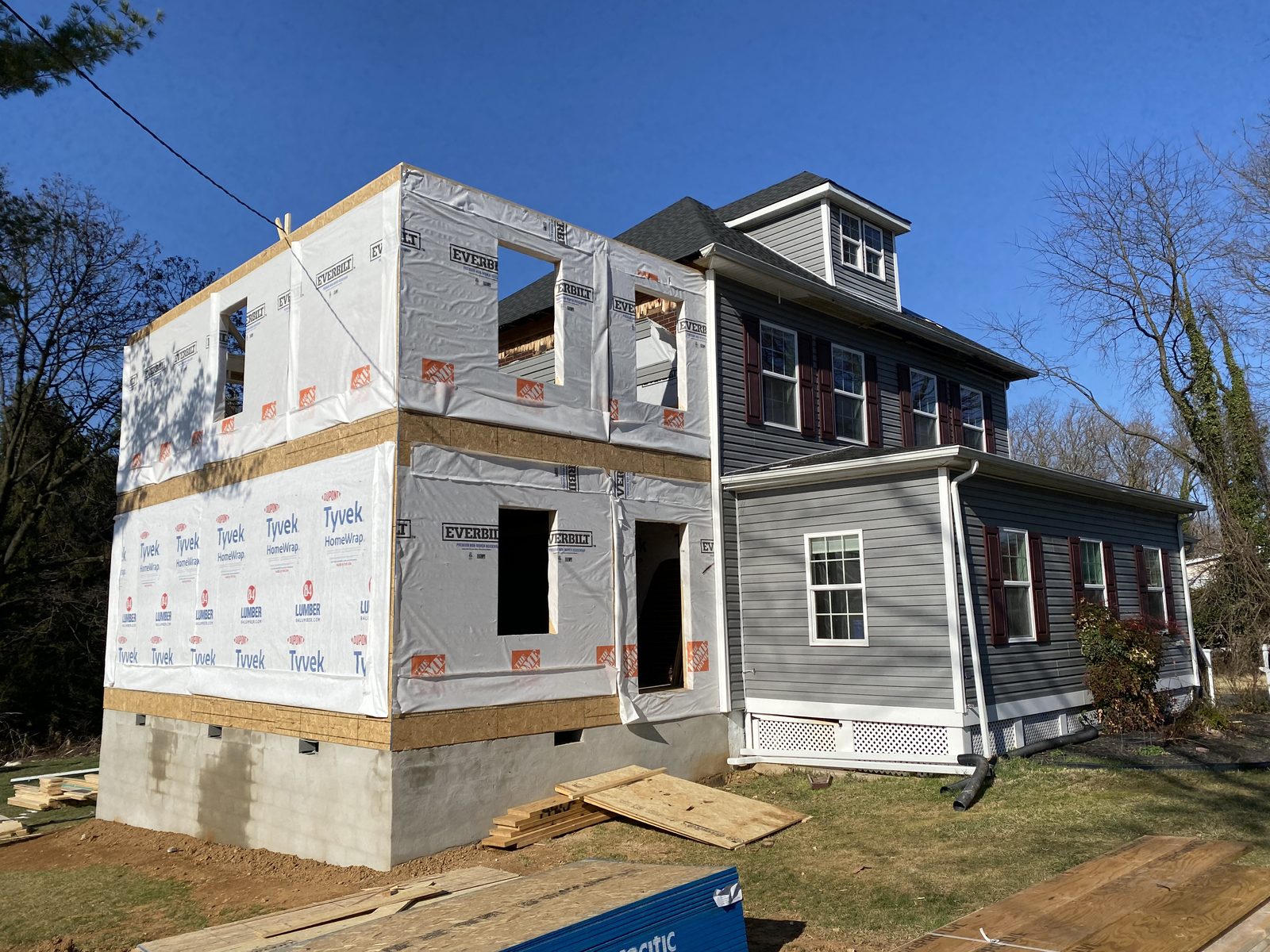 Two-story addition under housewrap attached to an existing gray home