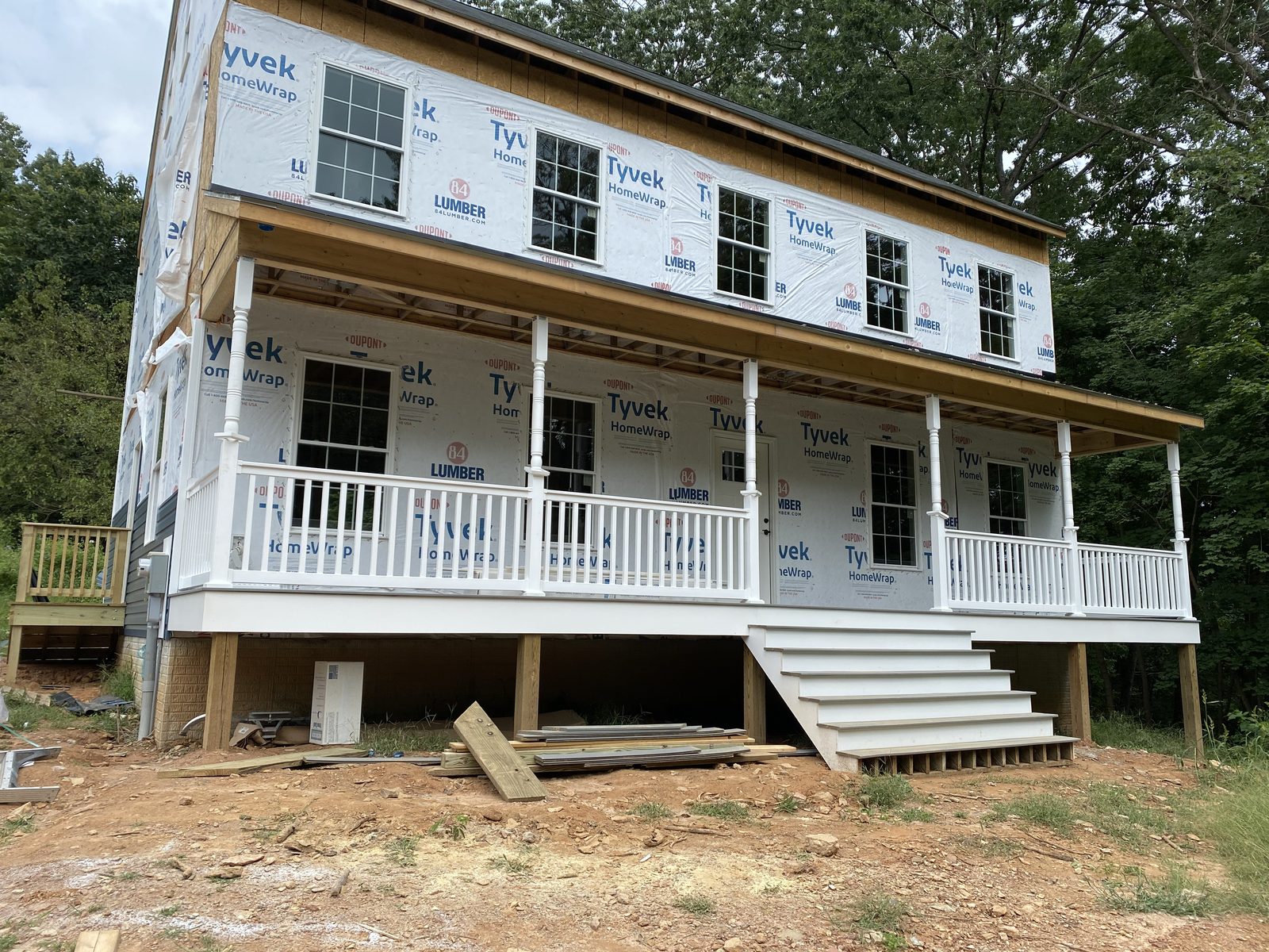 New wraparound porch with white railings and turned posts on a house still in wrap